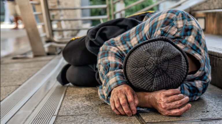 Imagem de um homem em situação de rua, dormindo em uma calçada.