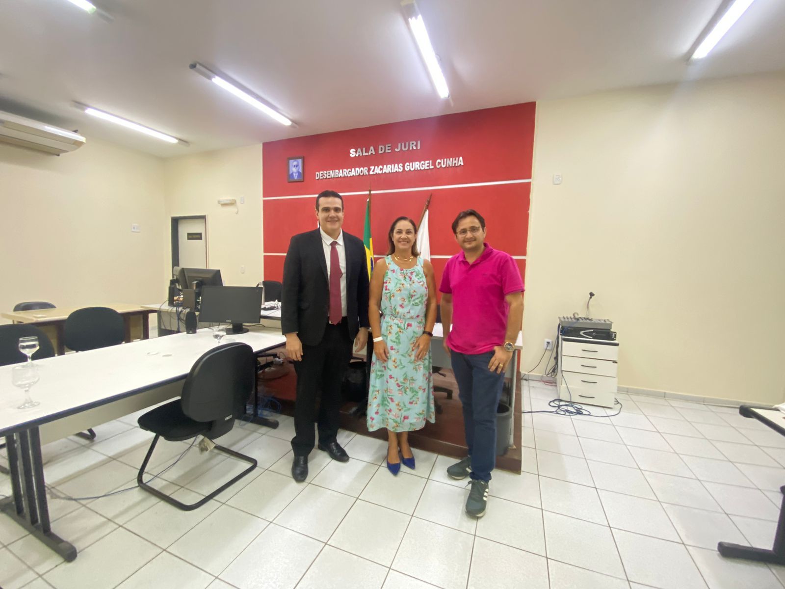 Imagem de três pessoas, sendo dois homens e uma mulher, em pé, posando para uma foto, em uma sala.