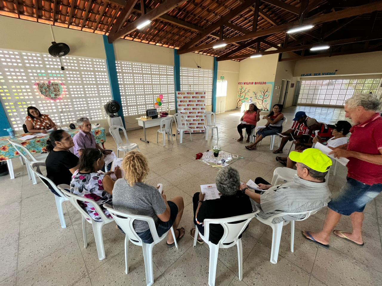 Imagem de várias pessoas idosas sentadas em cadeiras, dispostas em um círculo, durante uma atividade em grupo.