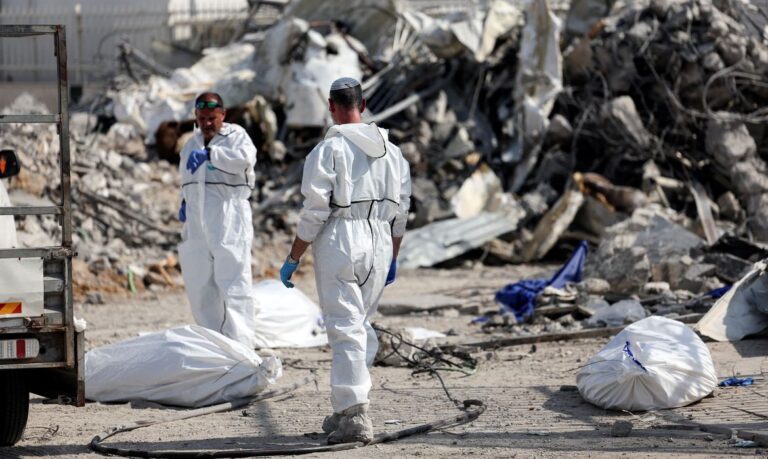 Israeli rescue workers work to remove dead bodies from near a destroyed police station that was the site of a battle following a mass-infiltration by Hamas gunmen from the Gaza Strip, In Sderot