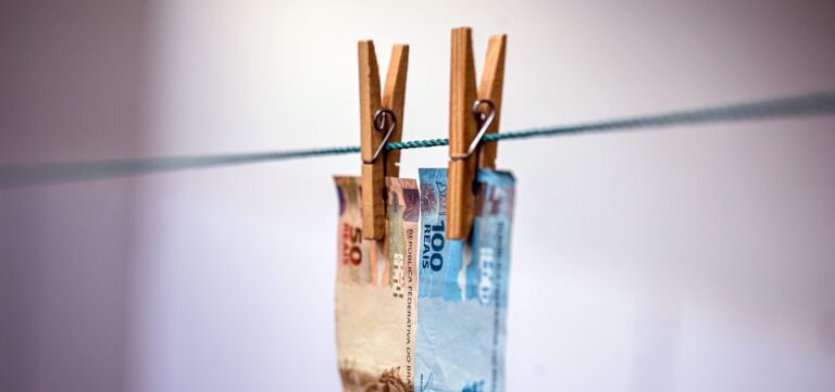 Imagem de duas notas de dinheiro, uma de 50 reais e outra de 100 reais, penduradas em um varal, com pegadores.