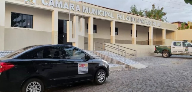 Imagem de um veículo preto, com adesivo do MPRN, estacionado em frente à Câmara Municipal de Vereadores de Santana do Matos.