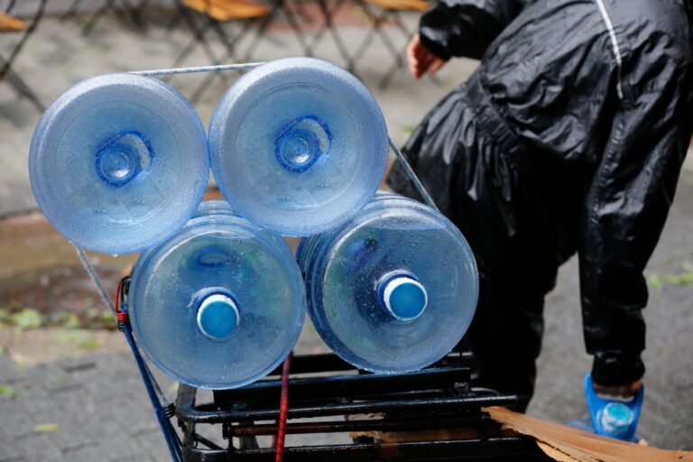 Imagem de quatro garrafões de água mineral sendo carregadas em um carrinho