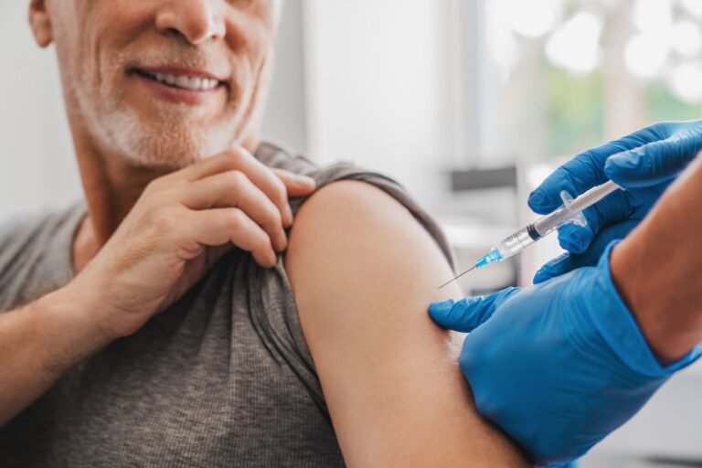 Imagem mostrando homem idoso recebendo vacina no braço com aplicação através de agulha.