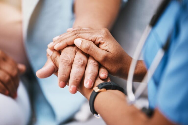 Imagem mostrando a mão de um profissional de saúde segurando a mão de um paciente