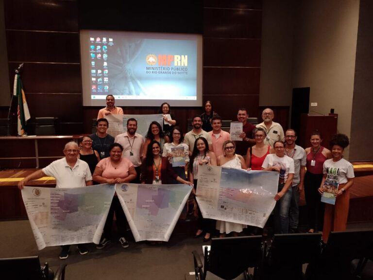 Imagem mostra as pessoas que participaram da reuniçao em pé, juntas, segurando as cartografias e os documentos apresentados
