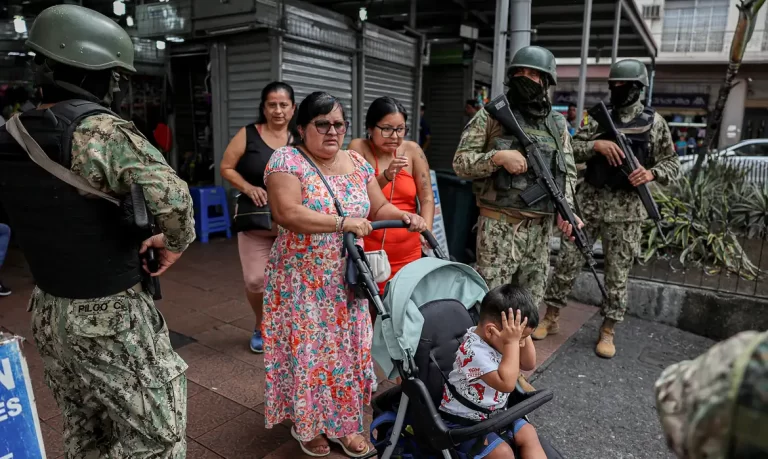 People walk past armed soldiers, as they guard a commercial area, in the aftermath of a wave a violence that saw the storming of a TV station on-air and explosions around the nation, in Quito, Ecuador, January 11, 2024. REUTERS/Ivan Alvarado