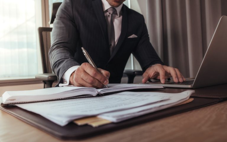 Imagem de um homem, vestido com terno e gravata, assinando um documento