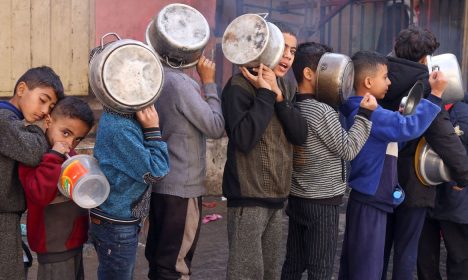 Crianças palestinas carregam panelas enquanto fazem fila para receber comida preparada em uma cozinha de caridade, em Rafah, no sul da Faixa de Gaza. 14/12/2023. REUTERS/Saleh Salem