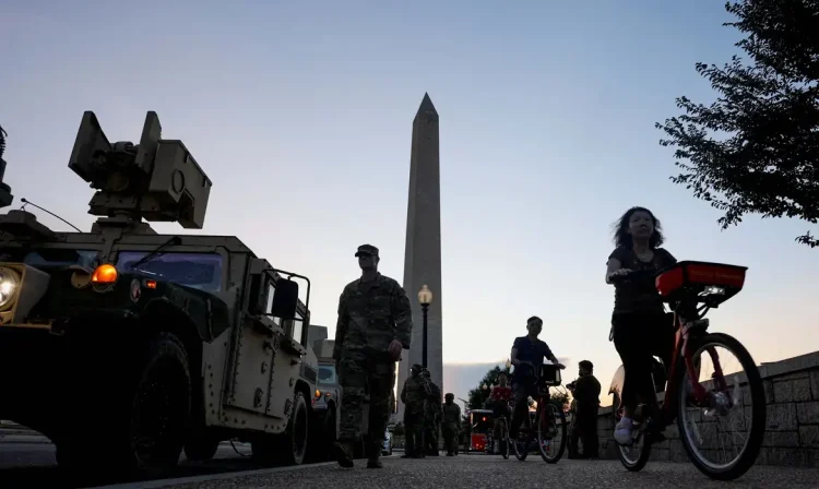 Tourists ride bicycles past U.S. Army National Guard Humvees near the Washington Monument after U.S. President Donald Trump announced a federal takeover of the Metropolitan Police Department under the Home Rule Act to assist with crime prevention in the nation's capital, Washington, D.C., U.S., August 12, 2025. REUTERS/Jonathan Ernst