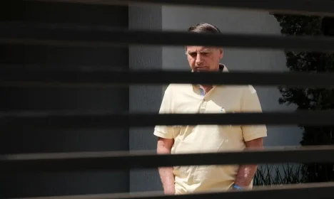 Brazil's former President Jair Bolsonaro stands at his home while under house arrest, amid the final phase of his trial, accused of plotting a coup after his electoral defeat, in Brasilia, Brazil, September 3, 2025. REUTERS/Diego Herculano   REFILE - CORRECTING DATE FROM