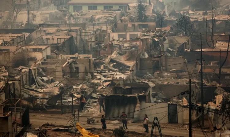 People stand among charred and heavily damaged properties in Concepcion, Chile, in the aftermath of a forest fire in the Biobio region, where, according to local media, multiple wildfires prompted emergency evacuations, January 18, 2026. REUTERS/Juan Gonzalez