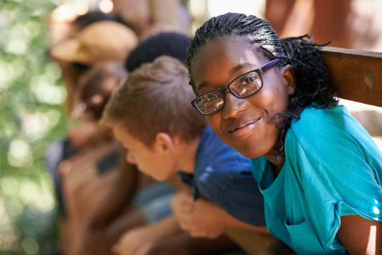 Imagem de uma adolescente negra, sorrindo, em primeiro plano, e crianças em segundo plano.