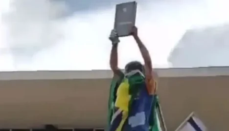 Homem levanta réplica da Constituição durante atos criminosos de 8 de janeiro. Foto: Reprodução