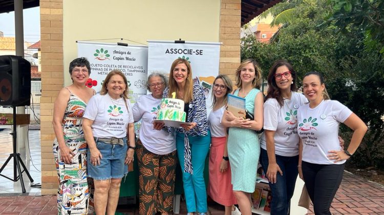 Imagem de oito mulheres, posicionadas lado a lado e uma delas segurando um bolo de aniversário.