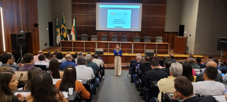 Imagem de uma mulher falando para uma plateia, em um auditório com várias pessoas.