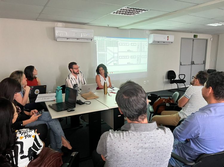 Imagem de pessoas reunidas ao redor de uma mesa, assistindo a um apresentação em um datashow.